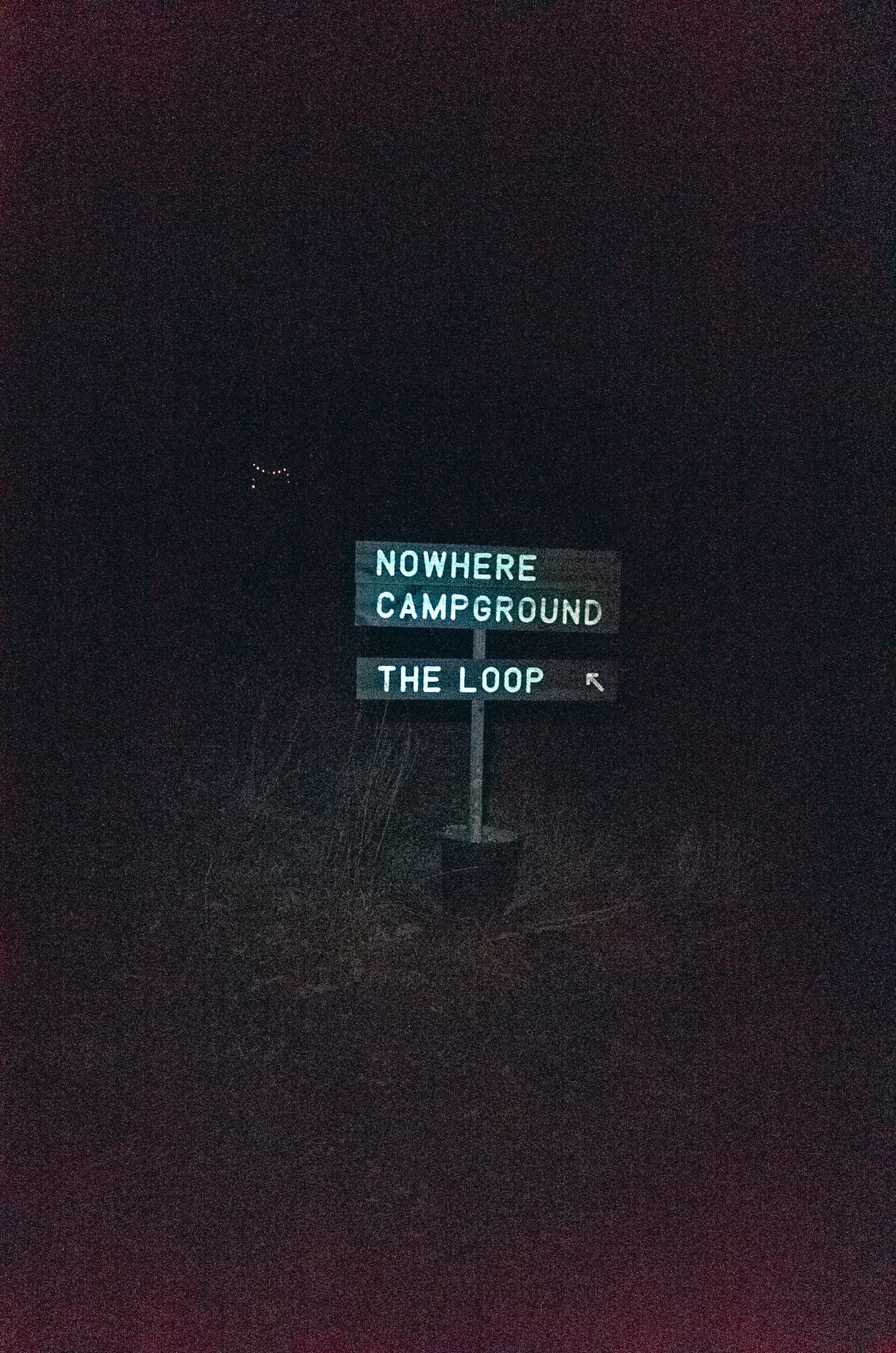 A wooden signpost reading Nowhere Campground, The Loop, lit at night